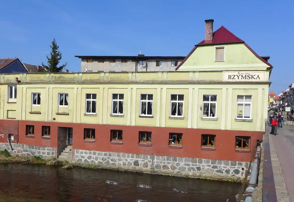 Żółta kamienica Karczmy Rzymskiej z szyldem RZYMSKA na brzegu Wieprzy