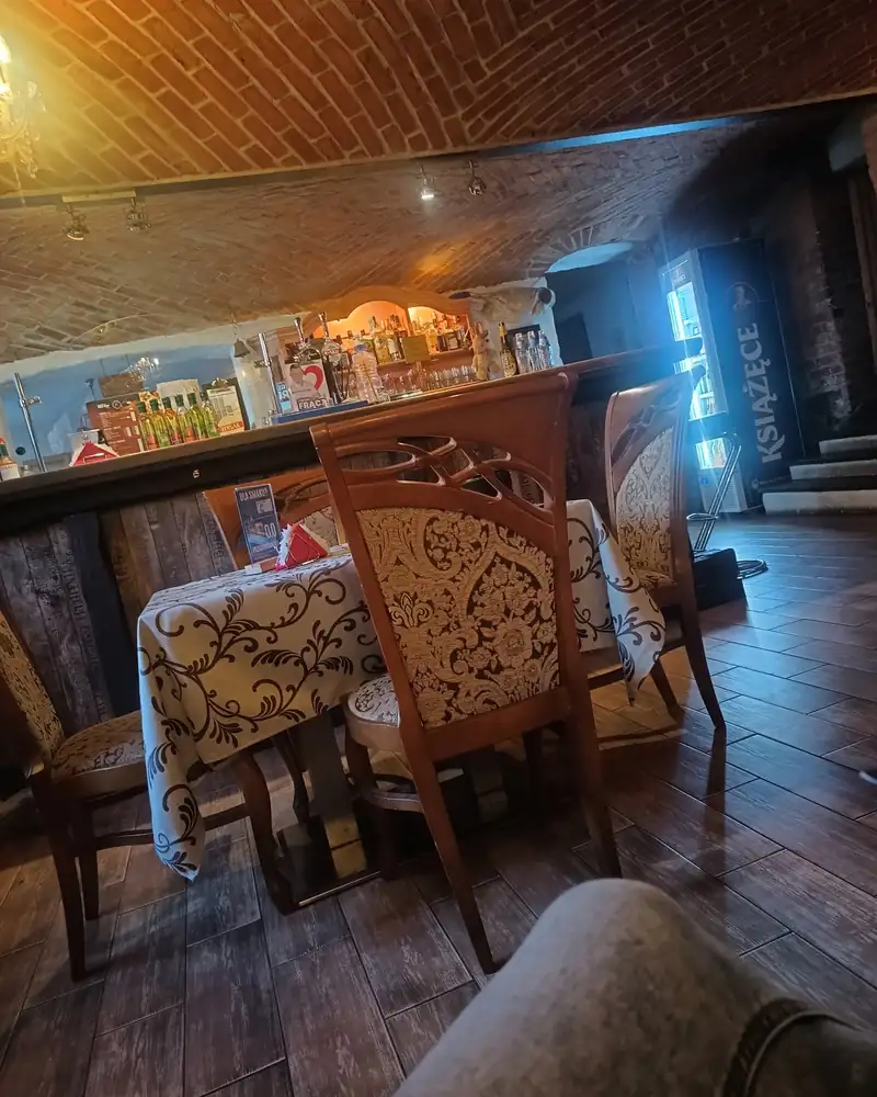Sala z drewnianą podłogą, krzesłami obitymi adamaszkiem i barem pod ceglanym sklepieniem